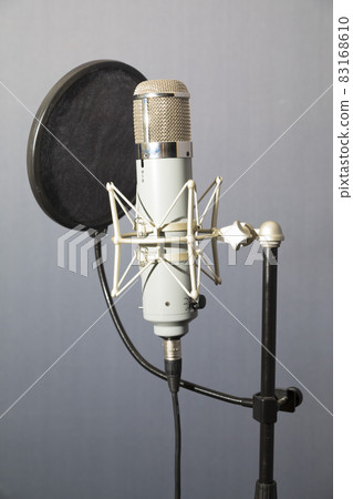 Studio microphone and pop shield on mic stand against gray background 83168610