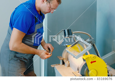 The turner sharpens the part on a grinding machine in the workshop. An adult man of 50 years in The turner sharpens the part on a grinding machine in the workshop. An adult man of 50 years in 83169076