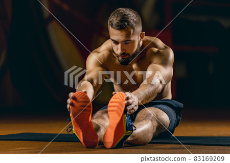Full-length portrait of young sportive man doing stretching. Gym training Full-length portrait of young sportive man doing stretching. Gym training 83169209