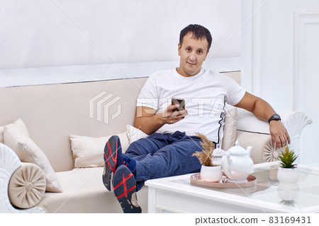 Mixed race man lies on couch with mobile phone. 83169431