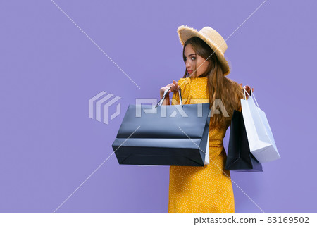 Back view of woman holds packages after shopping on purple background. discount, black Friday, sales 83169502