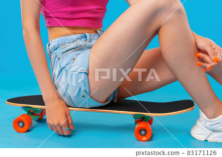 Pretty happy woman casually dressed sits on her skateboard Pretty happy woman casually dressed sits on her skateboard 83171126