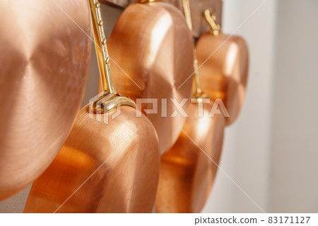Row of shiny clean copper pans, different size, hung on wooden plank Row of shiny clean copper pans, different size, hung on wooden plank 83171127