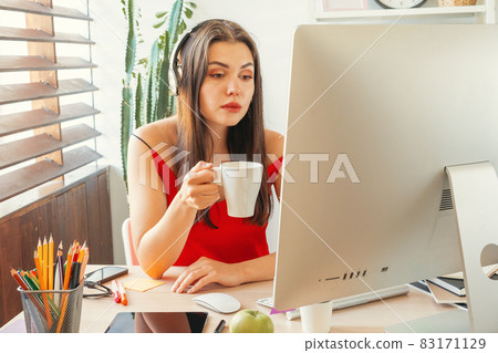 Young woman having a coffee break while sitting in her office Young woman having a coffee break while sitting in her office 83171129