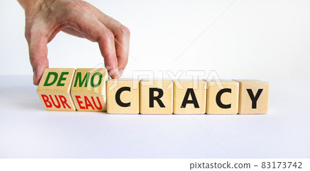 Democracy or bureaucracy symbol. Businessman turns wooden cubes and changes the word bureaucracy to democracy. Beautiful white background, copy space. Business and democracy or bureaucracy concept. 83173742