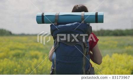 Young millennial girl travels with backpack and tourist rug, bright day in life, happy vacation concept, nature vacation on tourist road, looking for adventure on vacation, traveler concept 83173967