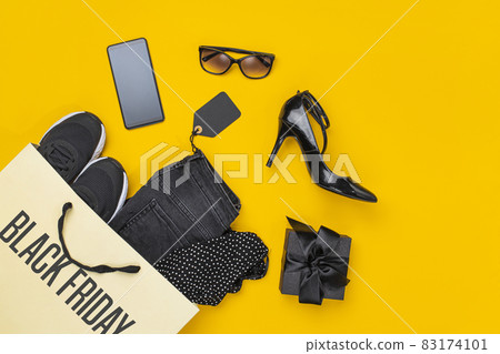 Paper shopping bag with clothes spill out on yellow background. Black friday concept. 83174101
