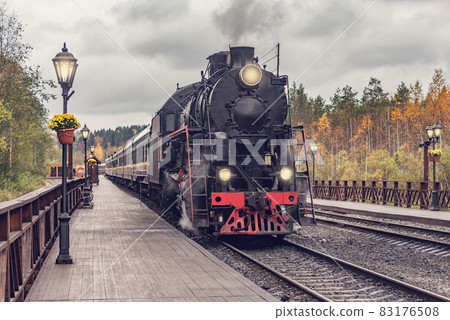 Retro steam train departs from the station wooden platform. Retro steam train departs from the station wooden platform. 83176508
