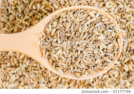 Dried fennel seeds in wooden spoon. 83177786