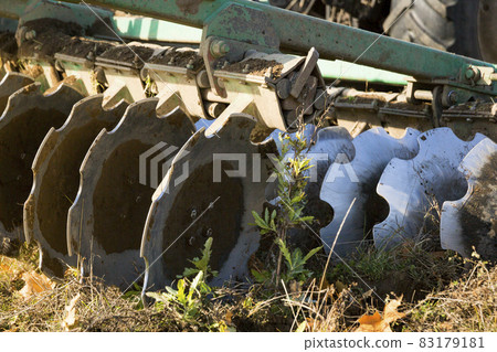 A farmer in a tractor, agricultural machinery, prepares the land with a cultivator. A modern red tractor in a field. Plowing a heavy tractor while cultivating agricultural work in a field with a plow. 83179181