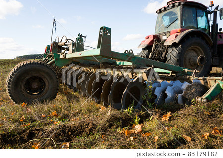 A farmer in a tractor, agricultural machinery, prepares the land with a cultivator. A modern red tractor in a field. Plowing a heavy tractor while cultivating agricultural work in a field with a plow. A farmer in a tractor, agricultural machinery, prepares the land with a cultivator. A modern red tractor in a field. Plowing a heavy tractor while cultivating agricultural work in a field with a plow. 83179182