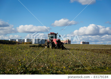 A farmer in a tractor, agricultural machinery, prepares the land with a cultivator. A modern red tractor in a field. Plowing a heavy tractor while cultivating agricultural work in a field with a plow. 83179184