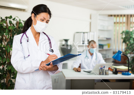 Doctor assistant in mask standing in office Doctor assistant in mask standing in office 83179413