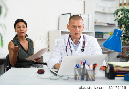 Doctor writing prescription to female patient on laptop at clinic Doctor writing prescription to female patient on laptop at clinic 83179416