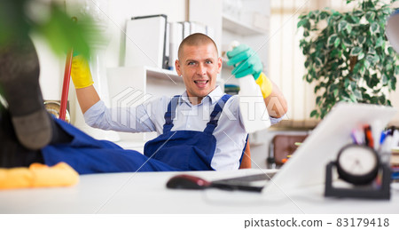 Relaxed cleaning service worker sitting in office with feet on table Relaxed cleaning service worker sitting in office with feet on table 83179418
