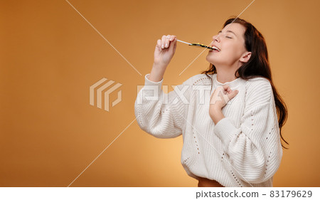 Woman enjoying biting green candy on yellow background. 83179629