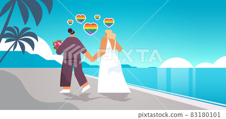 newlywed lesbian couple with flowers walking on beach transgender love LGBT community wedding celebration newlywed lesbian couple with flowers walking on beach transgender love LGBT community wedding celebration 83180101