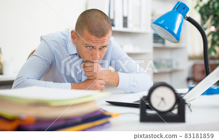 Focused businessman sitting at office table with chin on fists 83181859