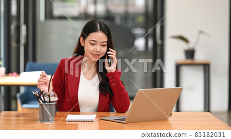 Confident businesswoman sitting at office desk and talking on mobile phone. 83182031