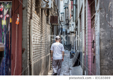 Hui Muslim ethnic minority man walking down a hutong street in Xian, China Hui Muslim ethnic minority man walking down a hutong street in Xian, China 83183869