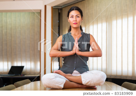 Businesswoman sitting at the table in lotus position Businesswoman sitting at the table in lotus position 83183909