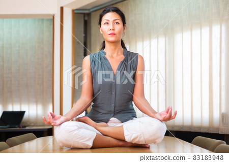 Businesswoman sitting at the table in lotus position Businesswoman sitting at the table in lotus position 83183948
