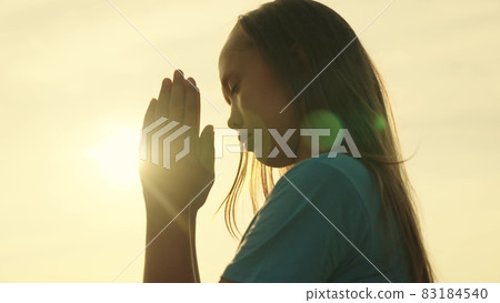 A Muslim girl prays in the glare of the sun in the sky, a little teenager believes in goodness, ask for forgiveness from heaven, educate a kid in religion, ask for good things in life, child dream of 83184540