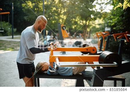 Father helps his son on exercise machine 83185084