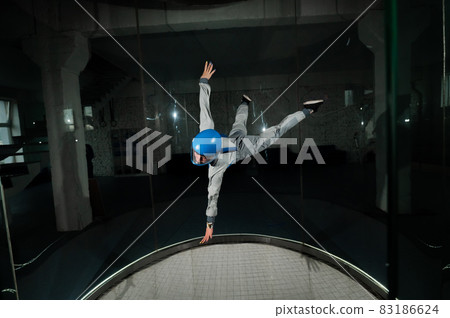 A young woman in overalls and a protective helmet enjoys flying in a wind tunnel. Free fall simulator A young woman in overalls and a protective helmet enjoys flying in a wind tunnel. Free fall simulator 83186624