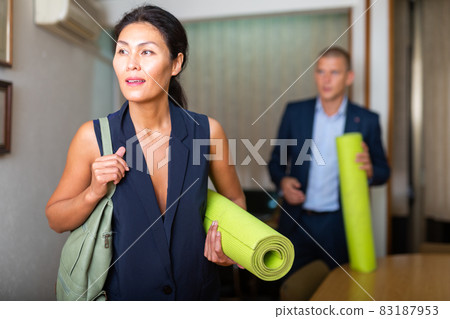 Smiling businesswoman standing in office with yoga matt 83187953