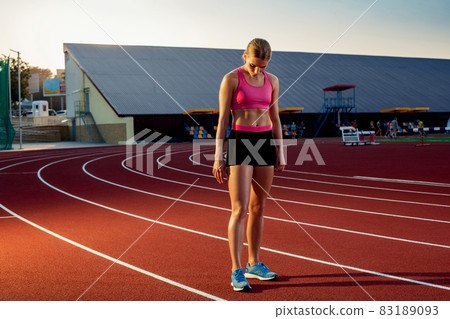 Picture of beautiful young European female runner or sprinter standing on outdoor stadium track, feeling exhausted after sprint or marathon. Picture of beautiful young European female runner or sprinter standing on outdoor stadium track, feeling exhausted after sprint or marathon. 83189093