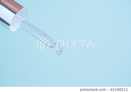 Transparent glass pipette with metallic lid, serum liquid dripping on blue background. 83190012