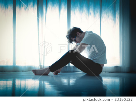 Hopeless caucasian man sitting alone by the window in silhouette with sadness on the floor. Hopeless caucasian man sitting alone by the window in silhouette with sadness on the floor. 83190122