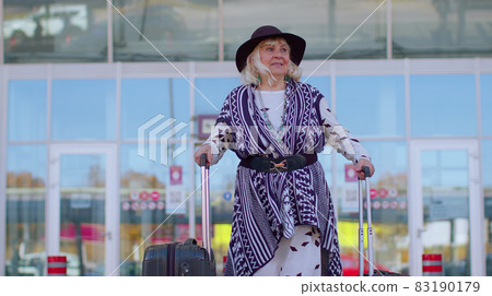 Senior pensioner tourist grandmother business woman walking from airport hall gate with luggage bag 83190179