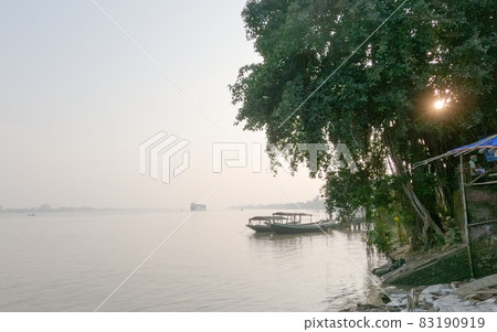 Horizon over river against clear sky in background and tree in the foreground of riverbank. Ganges riverside landscape view during sunset. Budge Budge West Bengal India 83190919