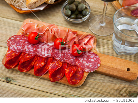 Spanish tasty meal slicing sausages and ham with tomatoes at wooden desk Spanish tasty meal slicing sausages and ham with tomatoes at wooden desk 83191302
