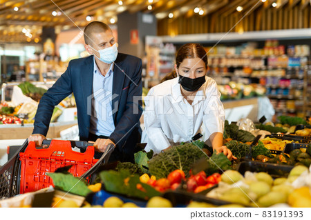 Young couple wearing protective masks in the supermarket chooses avocados 83191393