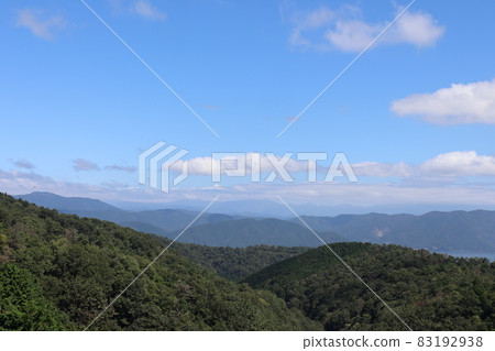 Mountains of various trees that can be clearly seen in the foreground, mountains that become hazy as you go farther, clouds and a landscape of blue sky 83192938