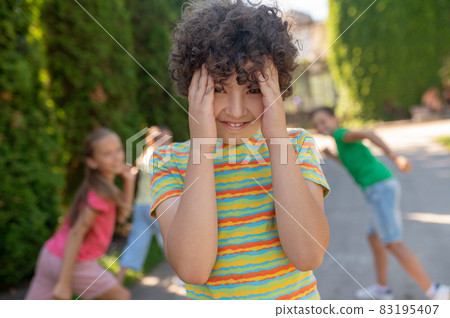 Smiling boy covering face with palms and hiding friends 83195407