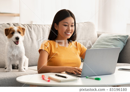 Cheerful japanese lady surfing on Internet, cute puppy sitting by Cheerful japanese lady surfing on Internet, cute puppy sitting by 83196180