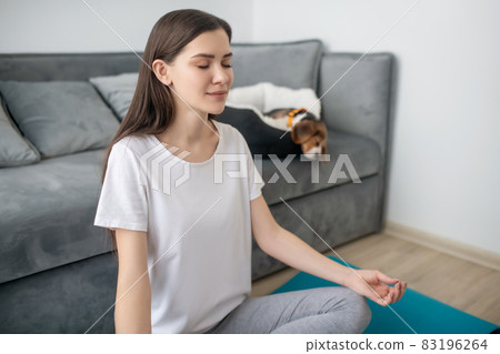 A woman sitting in a lotus pose while her puppy sleeping 83196264