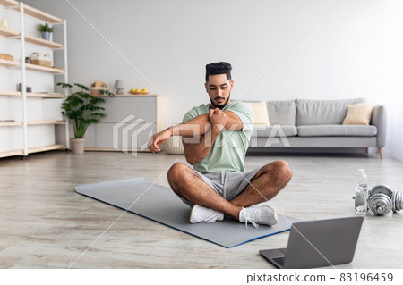 Athletic young Arab man doing yoga in front of laptop during home workout, copy space Athletic young Arab man doing yoga in front of laptop during home workout, copy space 83196459