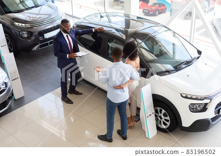 Professional Salesman Advertising New Car For Young Black Customers Couple In Showroom Professional Salesman Advertising New Car For Young Black Customers Couple In Showroom 83196502