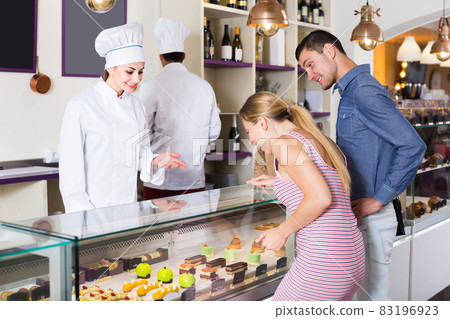 Chef woman is offering cakes from showcase Chef woman is offering cakes from showcase 83196923