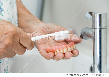 Asian senior or elderly old woman patient use toothbrush to clean partial denture of replacement teeth. Asian senior or elderly old woman patient use toothbrush to clean partial denture of replacement teeth. 83198113