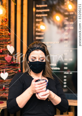 A sweet female of caucasian appearance in a black face mask, sits and works in an Internet cafe. A sweet female of caucasian appearance in a black face mask, sits and works in an Internet cafe. 83200251