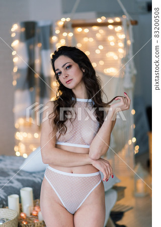 Beautiful female in lingerie near christmas fir in decorated studio 83200508