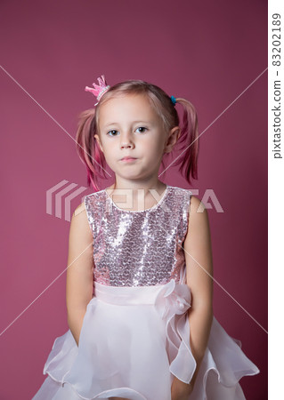 Little caucasian girl in a festive dress with sequins posing on a pink backgdrop Little caucasian girl in a festive dress with sequins posing on a pink backgdrop 83202189