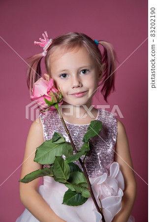 Little caucasian girl in a festive dress with sequins posing with rose flower Little caucasian girl in a festive dress with sequins posing with rose flower 83202190