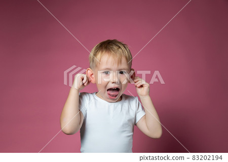 Caucasian boy makes faces, shows tongue, looking at camera on pink background 83202194